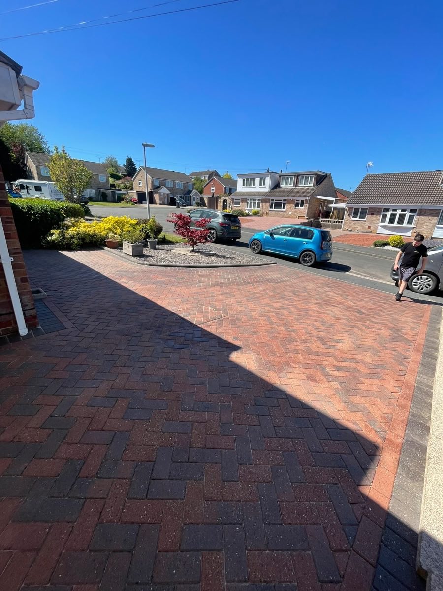 A red herringbone block driveway after cleaning, under blue sky