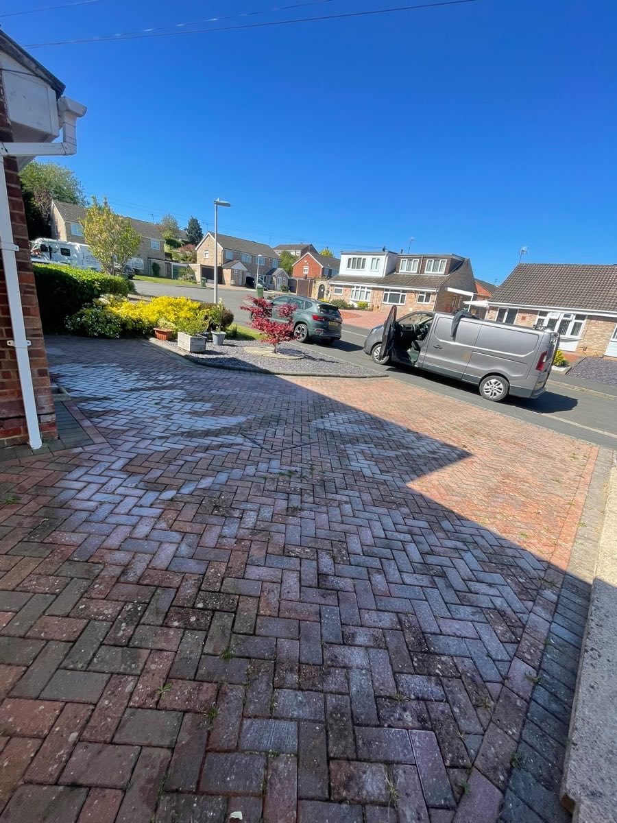 A red block driveway still wet from cleaning, with a van on the road