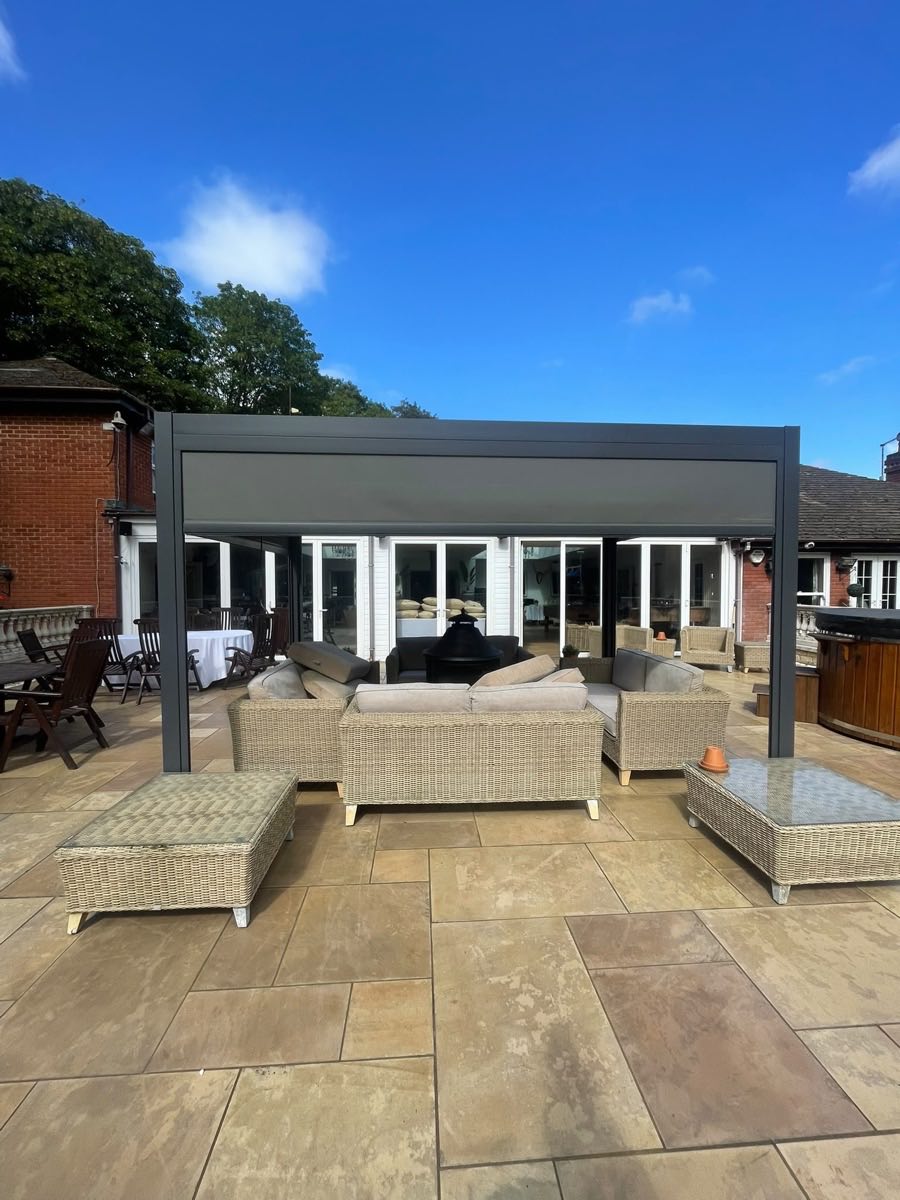A large sandstone patio after cleaning, with rattan furniture under a pergola and blue sky