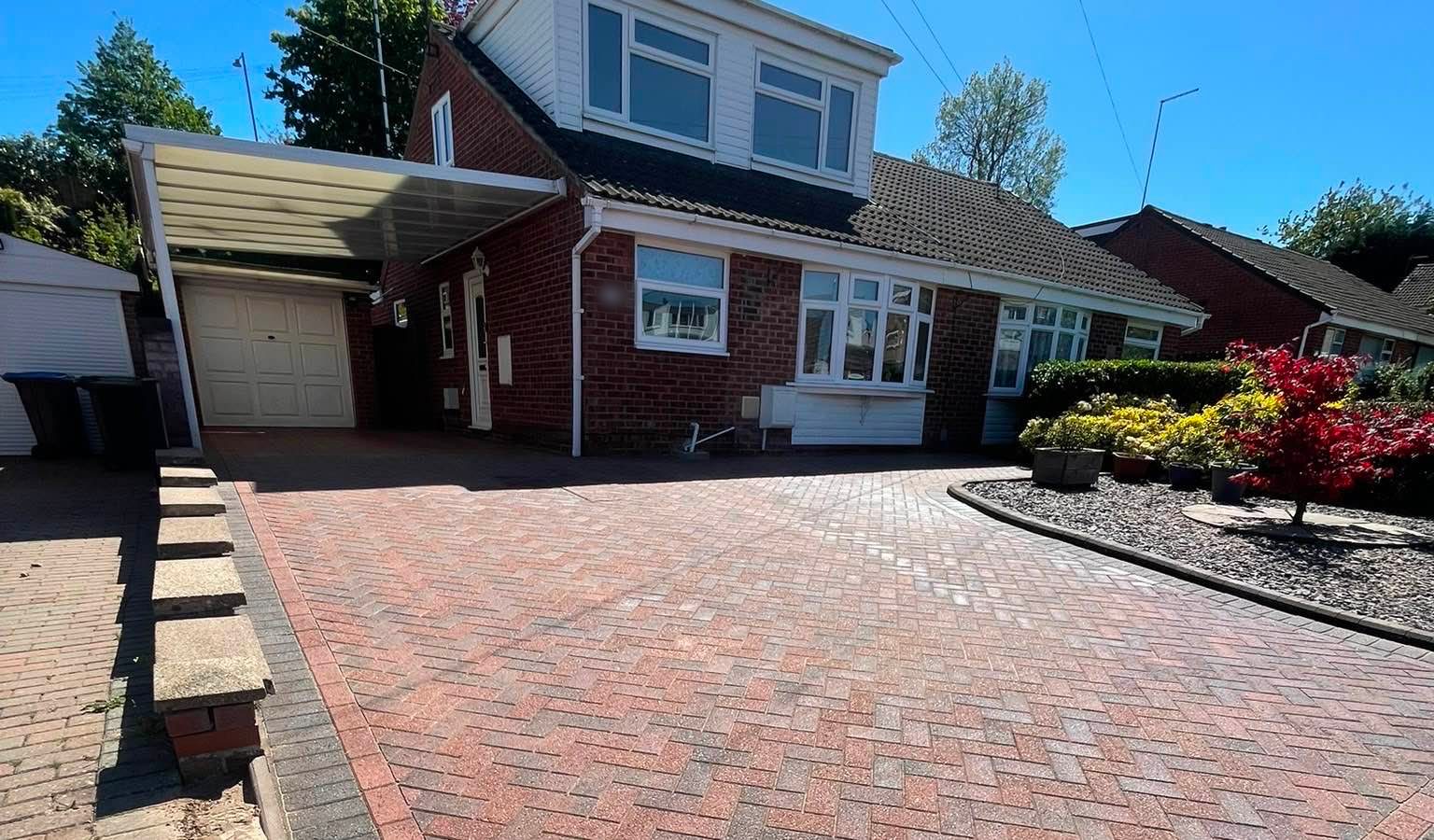 A block-paved driveway after cleaning, in bright sun, in front of a red brick house