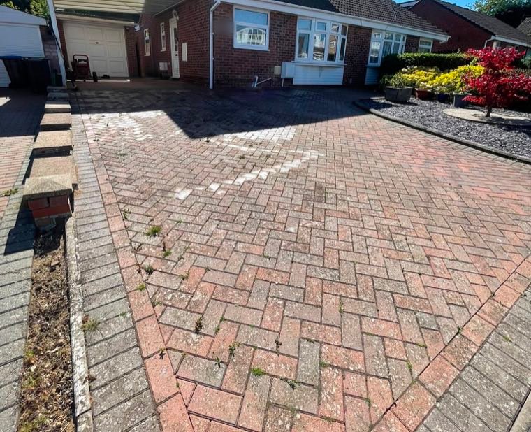 A block-paved driveway before cleaning, faded with weeds growing through the joints
