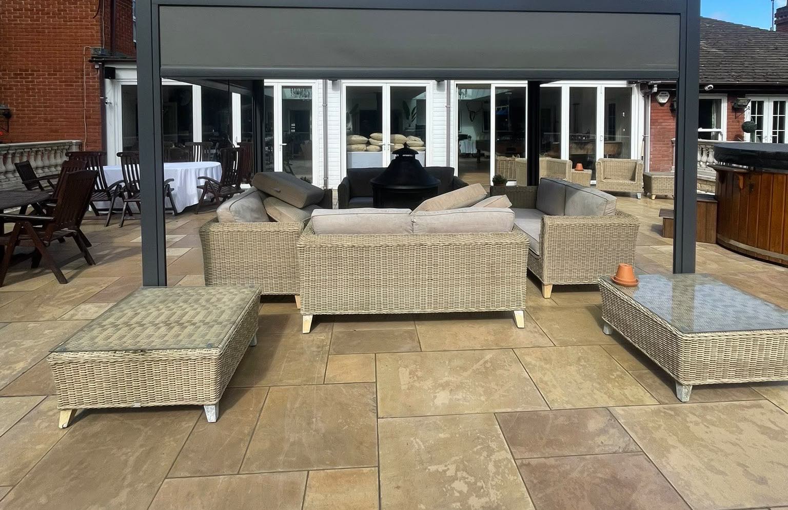 A large sandstone patio after cleaning, with furniture under a pergola
